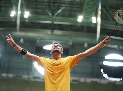 A badminton player in a yellow shirt celebrates triumphantly in an indoor stadium.