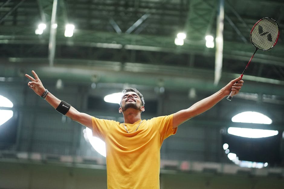 A badminton player in a yellow shirt celebrates triumphantly in an indoor stadium.