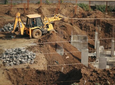 A bulldozer moves soil at a busy construction site, surrounded by piles of gravel and concrete structures. A bulldozer moves soil at a busy construction site, surrounded by piles of gravel and concrete structures.