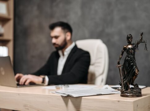 A businessman working on a laptop in an office with a Lady Justice statue in focus on the desk.