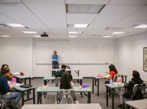 A classroom setting with a teacher proctoring an exam, students focused on their tests.