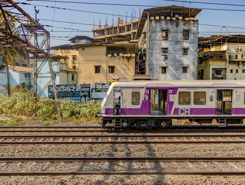 A colorful electric train travels through the urban landscape of Mumbai, India, showcasing vibrant architecture.