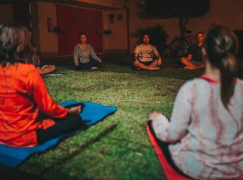 A group meditating cross-legged on grass during a peaceful evening outdoors. A group meditating cross-legged on grass during a peaceful evening outdoors.