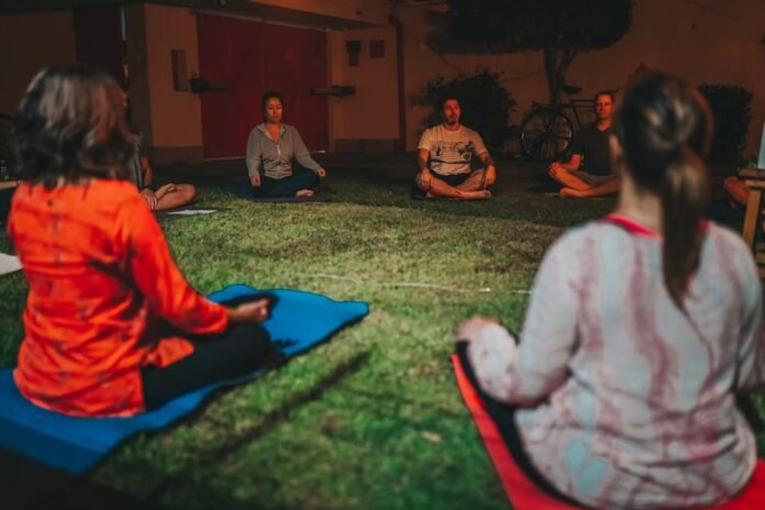 A group meditating cross-legged on grass during a peaceful evening outdoors. A group meditating cross-legged on grass during a peaceful evening outdoors.