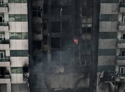 A high-rise building's facade shows severe fire damage with lingering smoke.