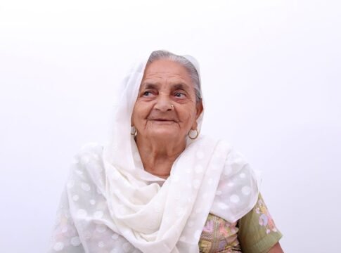A joyful senior woman smiling warmly in traditional clothing against a plain background.