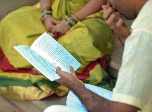A man and woman in traditional attire reading a book outdoors, showcasing cultural heritage.