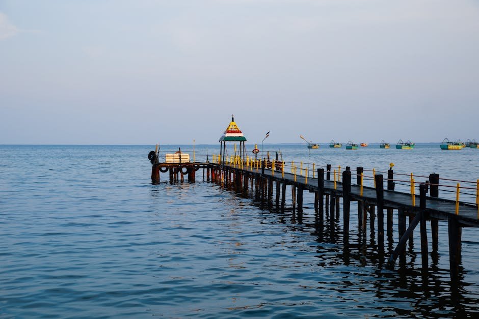 A peaceful view of a wooden boardwalk on Rameswaram's coastline featuring a colorful gazebo and distant boats.