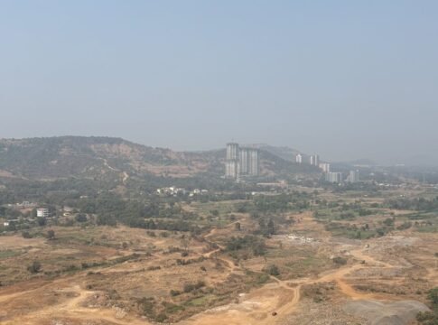 A scenic view of Pune's countryside with hills and high-rise buildings under a clear sky.