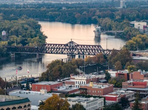 A scenic view of Sacramento's downtown riverfront featuring a historic bridge and colorful autumn foliage. A scenic view of Sacramento's downtown riverfront featuring a historic bridge and colorful autumn foliage.