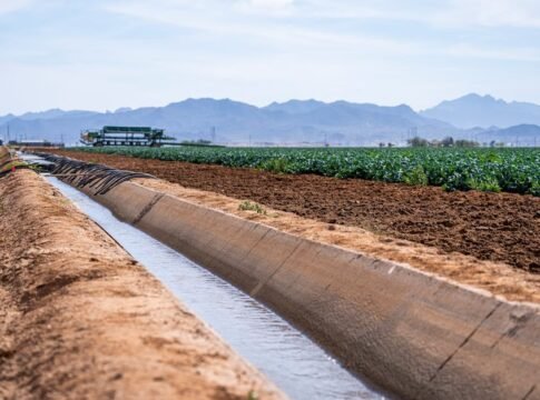 A scenic view of an irrigation canal running through farmland with mountains in the background.