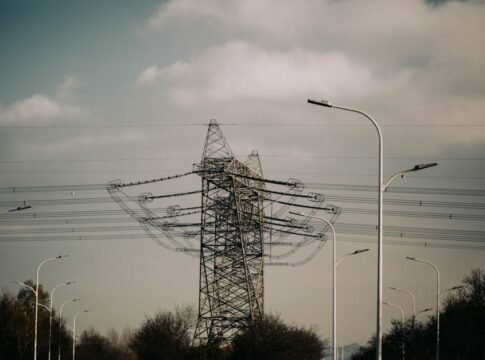 A scenic view of high voltage power lines and a lattice tower with surrounding streetlights under a cloudy sky. A scenic view of high voltage power lines and a lattice tower with surrounding streetlights under a cloudy sky.