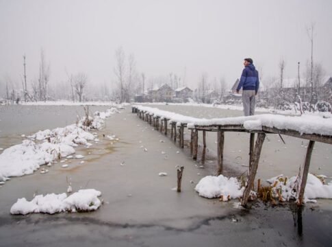 A serene winter scene in Kashmir with a snow-covered bridge and a person gazing into the distance.