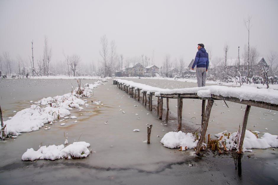 A serene winter scene in Kashmir with a snow-covered bridge and a person gazing into the distance.