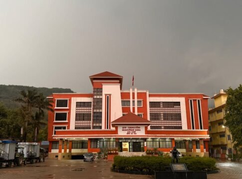 A striking red government building stands under an overcast sky, featuring modern architecture.