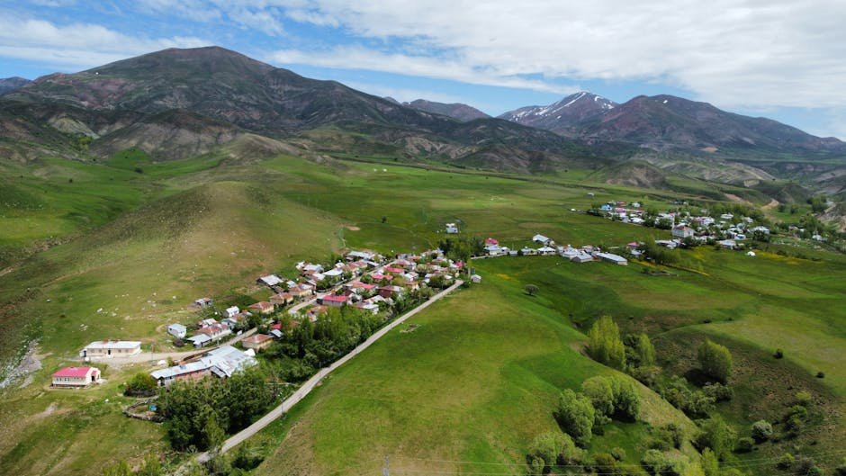 Jammu and Kashmir: Tree Fall Disrupts Traffic in Rajbagh A stunning aerial view of a remote village nestled in lush green hillsides, under a bright sky.