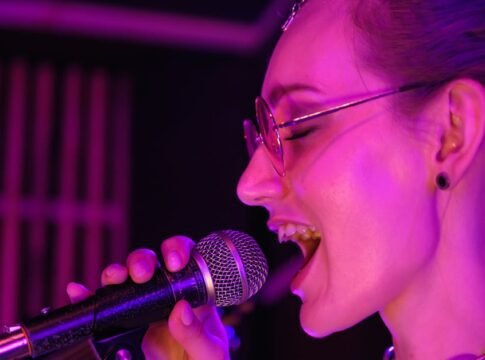 A vibrant close-up of a female singer performing with passion under purple stage lights.