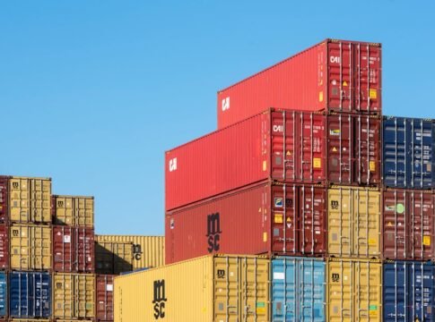 A vibrant collection of stacked shipping containers under a clear, blue sky. Ideal for logistic themes.