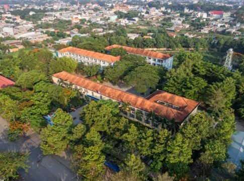 Aerial shot showcasing a city landscape with a prominent school building amidst green trees.