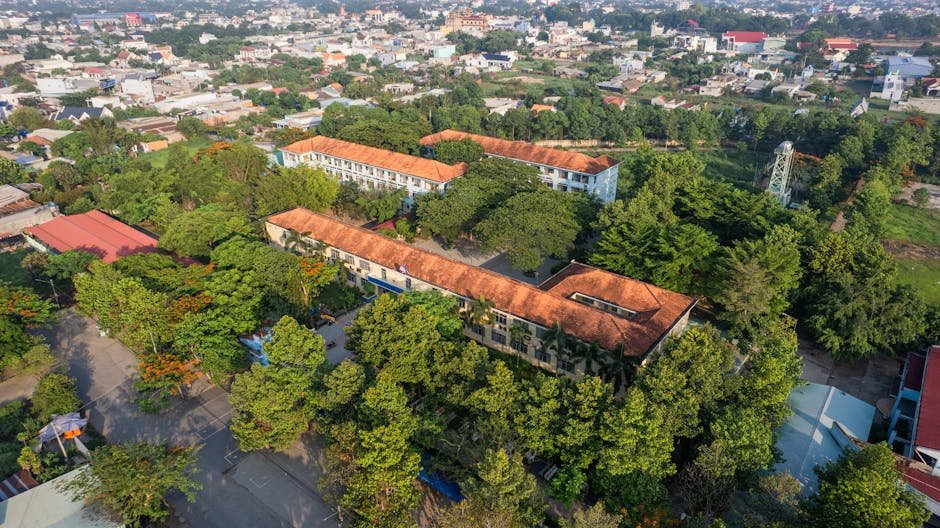 Aerial shot showcasing a city landscape with a prominent school building amidst green trees.
