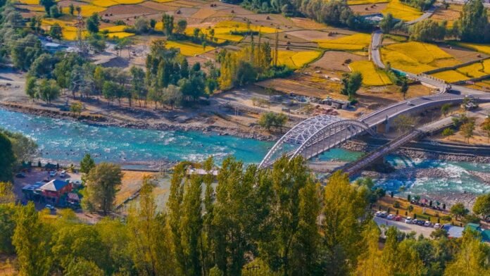 Aerial view of a picturesque bridge crossing a turquoise river in the rural fields of Ganderbal.