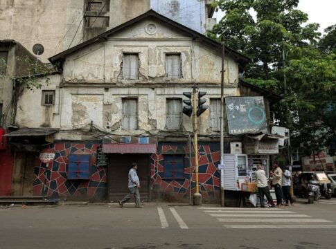 Aged building with vibrant mosaic facade on a busy street in Pune, India.