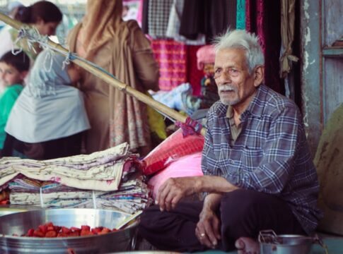 An elderly man selling textiles at a bustling market in Kashmir, India.