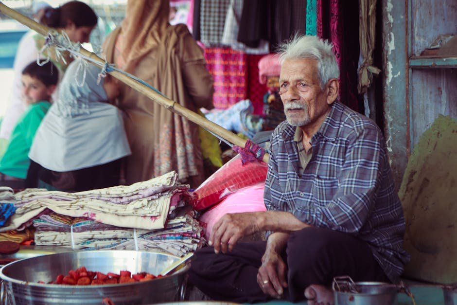 Jammu and Kashmir Artisans Showcase Traditional Crafts at ‘Know Your Artisan’ Exhibition An elderly man selling textiles at a bustling market in Kashmir, India.