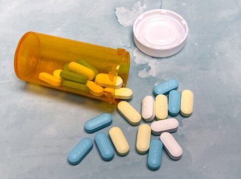 An open prescription bottle with assorted pills on a light blue background, high angle view. An open prescription bottle with assorted pills on a light blue background, high angle view.