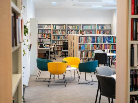 Bright library space featuring bookshelves, colorful chairs, and desks, ideal for studying and reading.