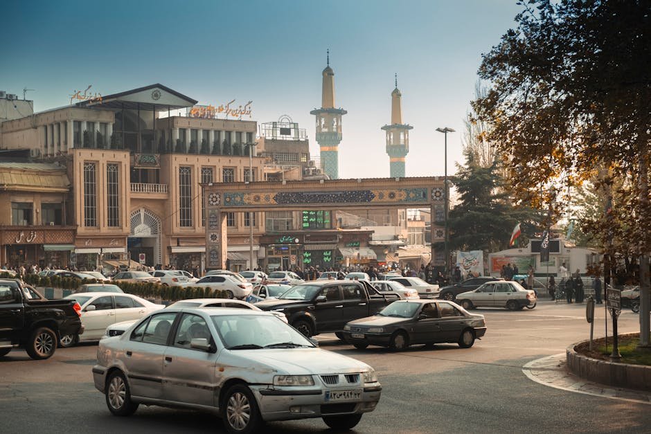 US and Iran Prepare for Pakistan Talks Amid Ceasefire, Key Issues Loom Bustling Tehran street scene with cars, mosque minarets, and traditional architecture.