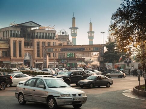 Bustling Tehran street scene with cars, mosque minarets, and traditional architecture.