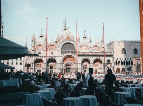 Capture of St. Mark's Basilica in Venice with outdoor seating and tourists on a sunny day.