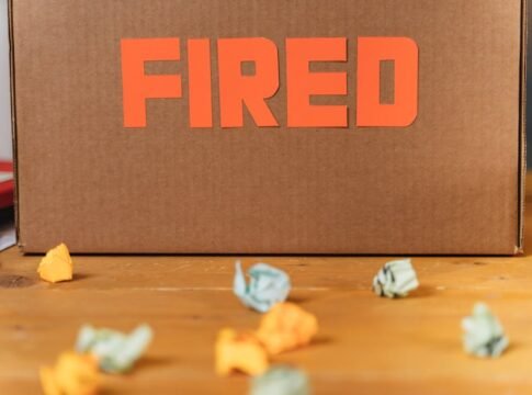 Close-up of a cardboard box labeled FIRED on a wooden table with crumpled papers. Close-up of a cardboard box labeled FIRED on a wooden table with crumpled papers.