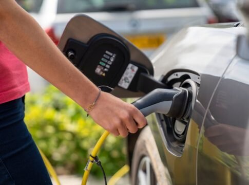 Close-up of a person plugging in an electric car at a charging station outdoors. Close-up of a person plugging in an electric car at a charging station outdoors.