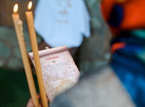 Close-up of a religious ceremony with lit candles and an Orthodox prayer scroll.