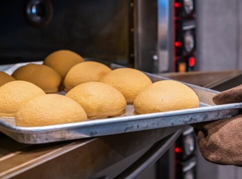 Close-up of freshly baked golden brown bread rolls on a stainless steel tray being removed from an oven. Close-up of freshly baked golden brown bread rolls on a stainless steel tray being removed from an oven.