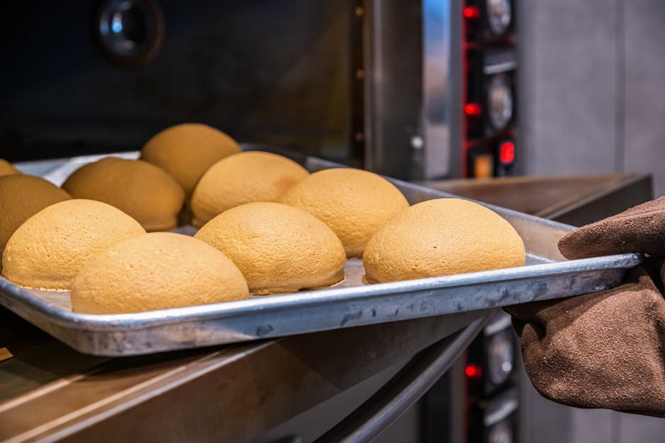 Mumbai Bakers Face Crisis as LPG Shortage Threatens Ladi Pav Production Close-up of freshly baked golden brown bread rolls on a stainless steel tray being removed from an oven.