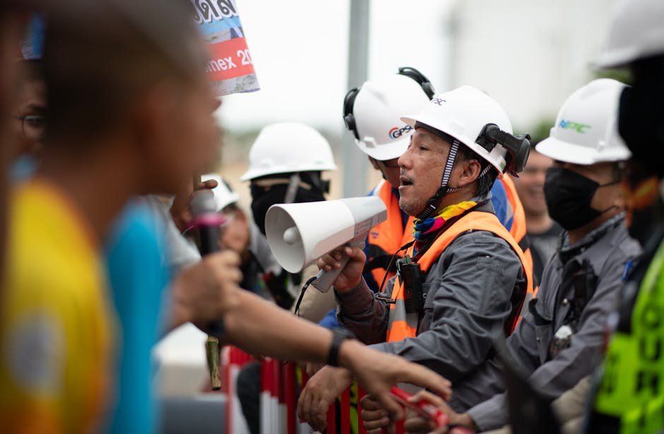 Noida Gridlock: Factory Worker Protest Paralyzes Highways, Strands Thousands Construction workers in a heated protest with security present. Safety and communication emphasized.