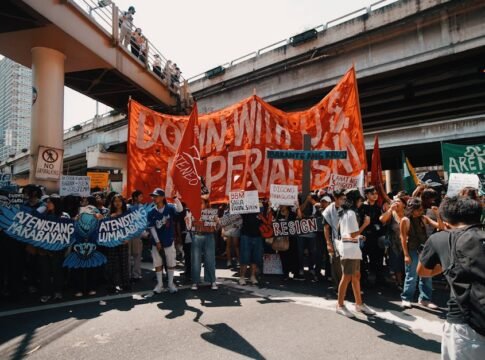 Crowd of protesters with banners under a city overpass during daytime.