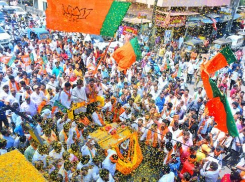 Crowds gather in Mangaluru for a colorful street parade with vibrant flags and decorations.