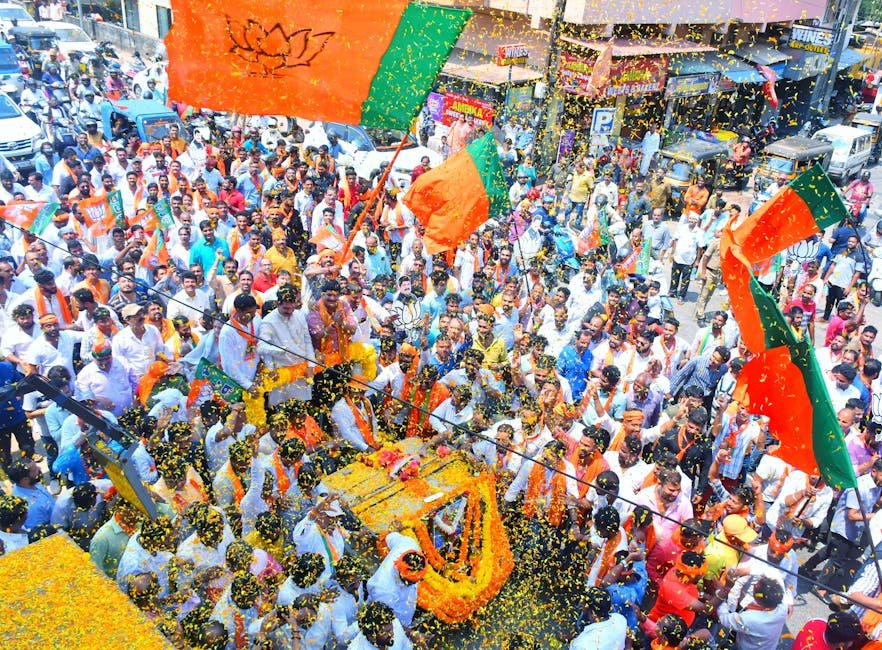Crowds gather in Mangaluru for a colorful street parade with vibrant flags and decorations.