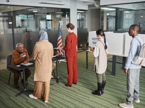 Diverse group of voters lining up at an indoor polling station on election day.