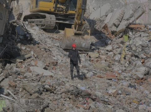 Excavator clearing urban demolition site rubble with a worker on site. Excavator clearing urban demolition site rubble with a worker on site.