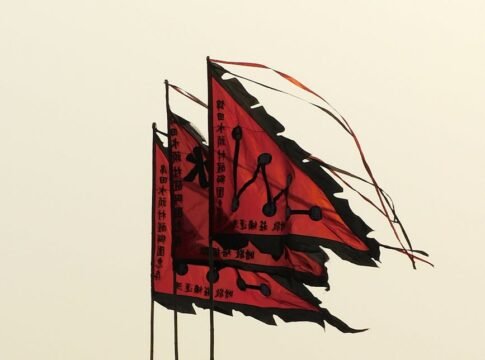 From below of similar red and black flags with hieroglyphs waving in wind against cloudy sky From below of similar red and black flags with hieroglyphs waving in wind against cloudy sky