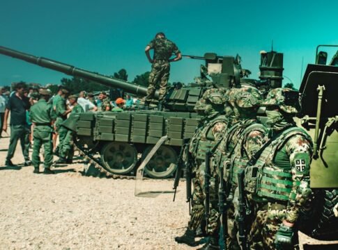 Group of camouflaged soldiers near a tank during a training exercise outdoors.