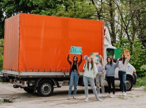 Group of young women protesting outdoors with signs and banners by a truck.