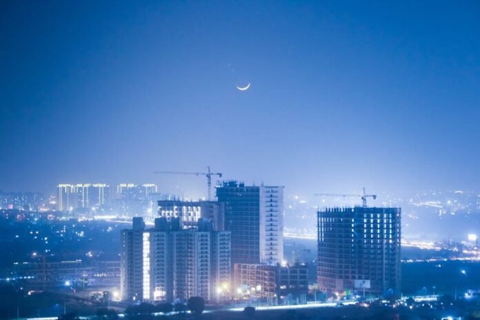 Illuminated cityscape of Greater Noida at night with a crescent moon enhancing the urban skyline. Illuminated cityscape of Greater Noida at night with a crescent moon enhancing the urban skyline.