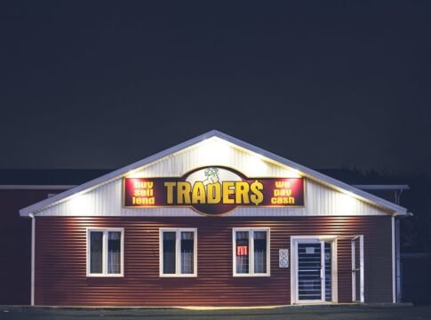 Illuminated trader's storefront at night displaying vibrant signage with business motifs.