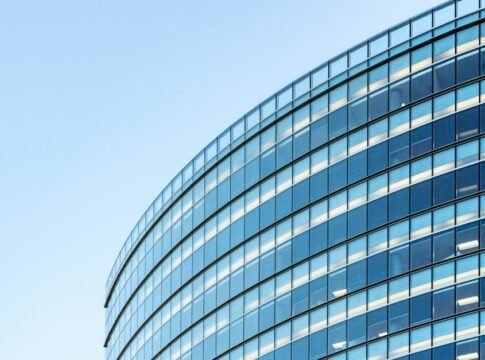 Low angle view of a modern glass office building against a clear blue sky.